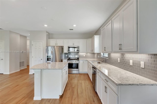 kitchen with visible vents, a kitchen island, stainless steel appliances, white cabinetry, and a sink