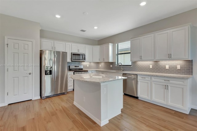 kitchen with light stone counters, a kitchen island, white cabinets, appliances with stainless steel finishes, and light wood-type flooring