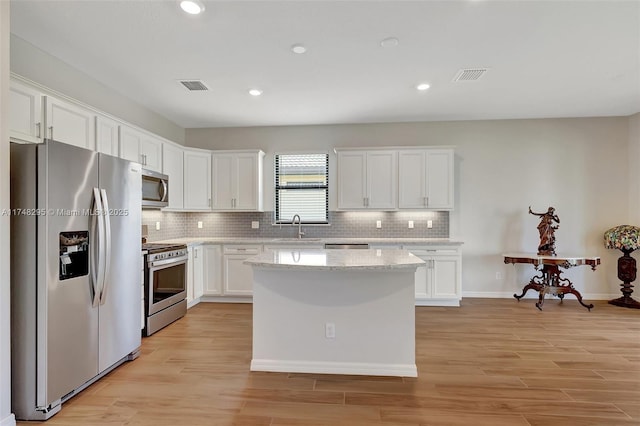 kitchen with visible vents, white cabinets, a center island, stainless steel appliances, and a sink