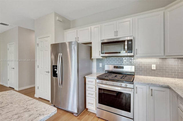 kitchen featuring light stone counters, stainless steel appliances, visible vents, backsplash, and white cabinets