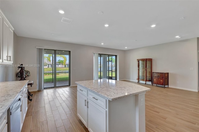 kitchen featuring light stone counters, stainless steel dishwasher, a kitchen island, and white cabinetry