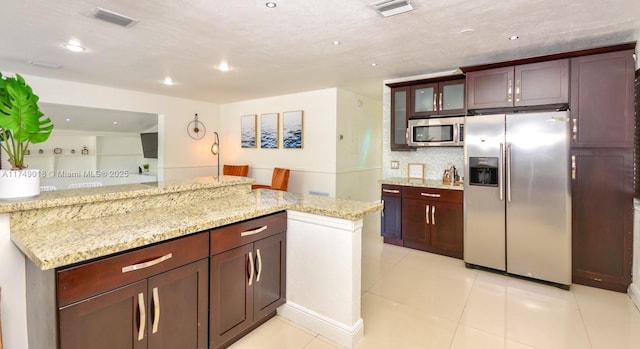 kitchen featuring light stone counters, light tile patterned floors, stainless steel appliances, visible vents, and glass insert cabinets