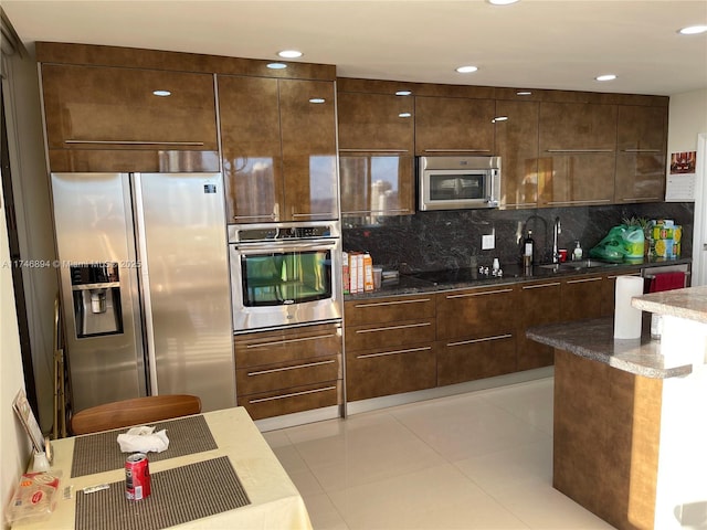 kitchen featuring light tile patterned floors, a sink, decorative backsplash, dark brown cabinets, and appliances with stainless steel finishes