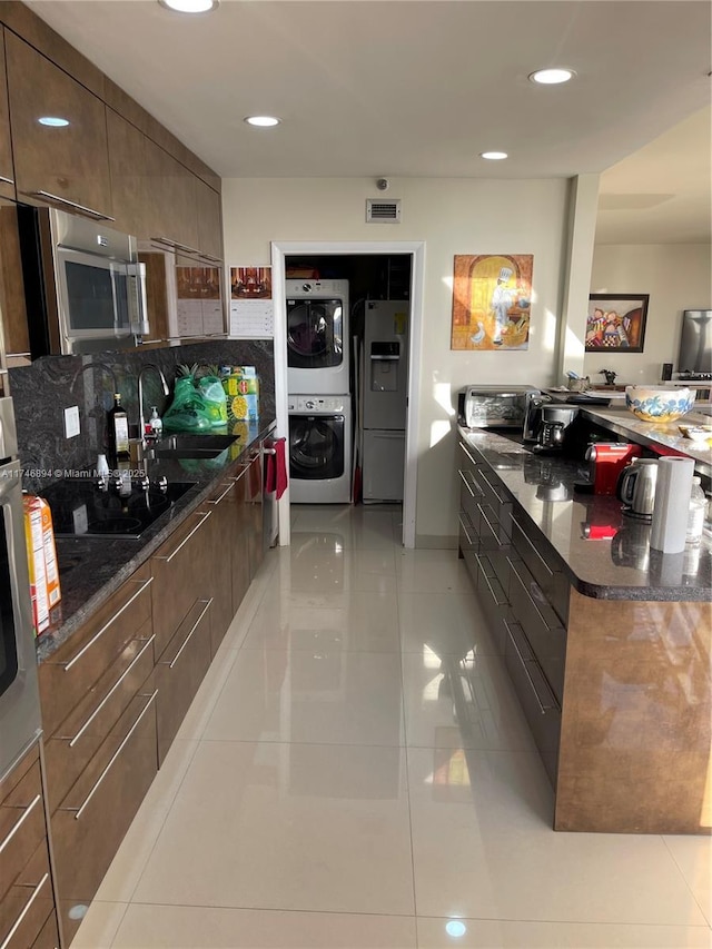 kitchen with refrigerator with ice dispenser, a sink, stainless steel microwave, stacked washer / dryer, and black electric cooktop