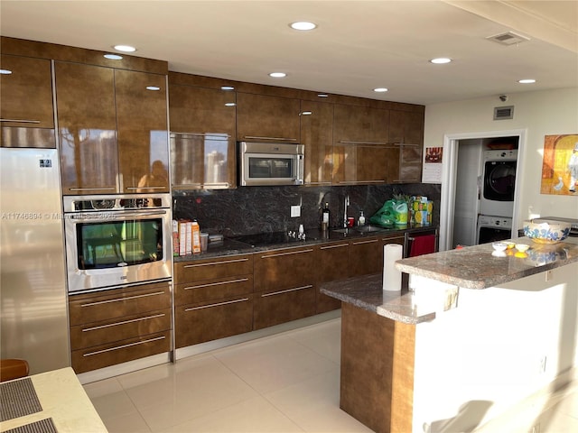 kitchen featuring stainless steel appliances, a sink, stacked washer / drying machine, dark stone countertops, and modern cabinets