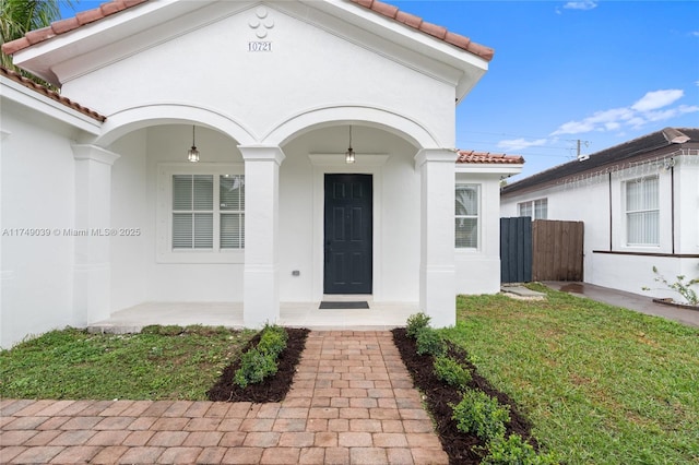 doorway to property featuring a tiled roof, a yard, fence, and stucco siding