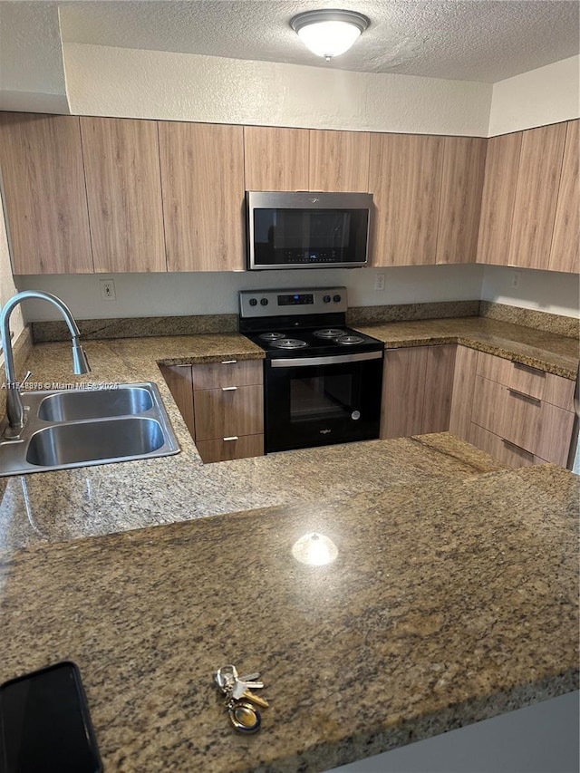 kitchen featuring brown cabinets, stainless steel microwave, electric range, a sink, and a textured ceiling