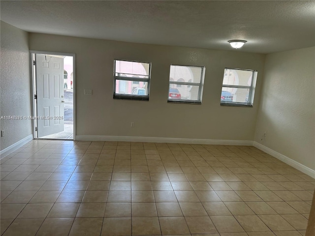 empty room with a textured ceiling, a textured wall, and baseboards