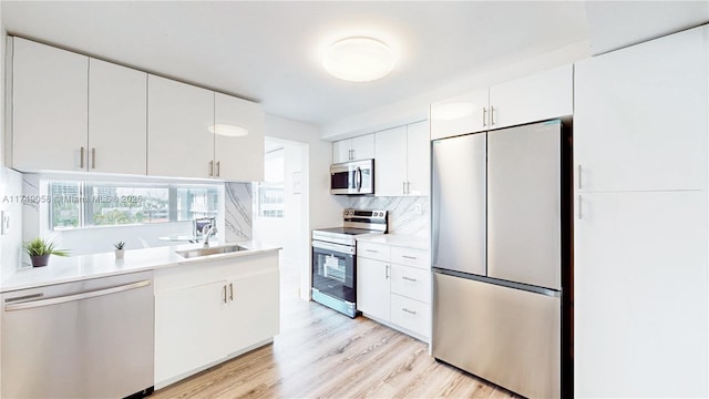 kitchen featuring light wood finished floors, stainless steel appliances, light countertops, white cabinetry, and a sink