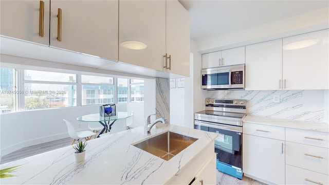 kitchen featuring white cabinets, decorative backsplash, appliances with stainless steel finishes, light stone counters, and a sink