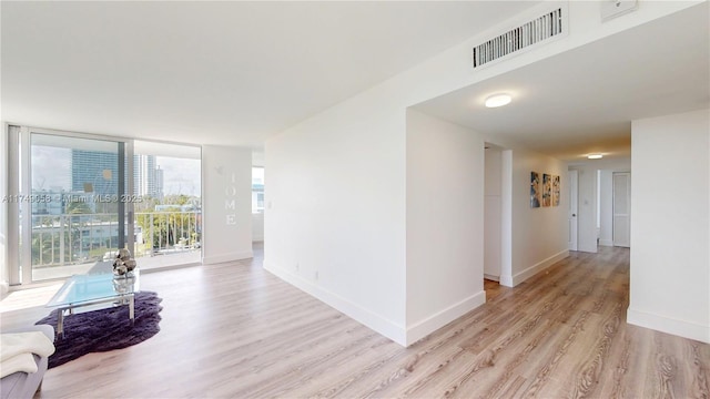 hallway featuring light wood-style flooring, a city view, visible vents, baseboards, and floor to ceiling windows