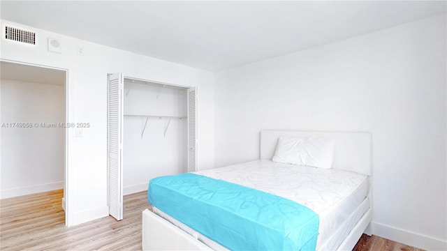 bedroom with baseboards, light wood-style flooring, visible vents, and a closet