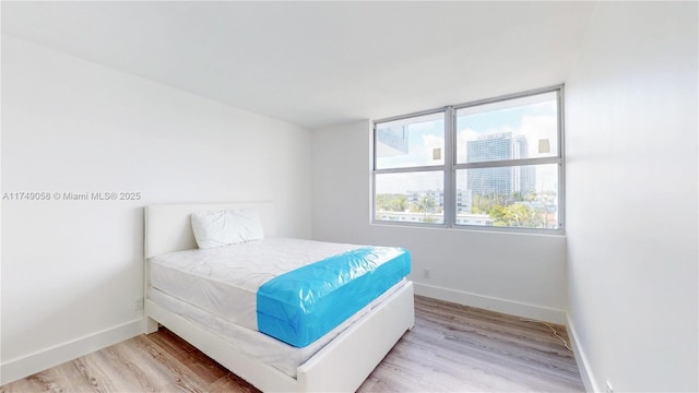 bedroom with light wood-type flooring, a view of city, and baseboards