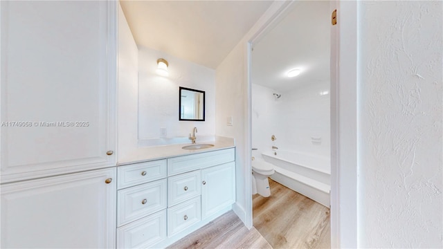 bathroom with toilet, a textured wall, wood finished floors, and vanity