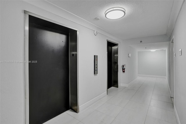 hallway featuring elevator, light tile patterned flooring, a textured ceiling, and baseboards