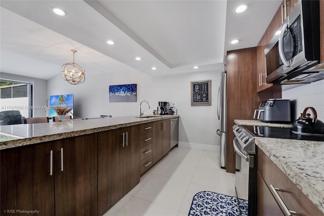 kitchen featuring light stone counters, a sink, open floor plan, appliances with stainless steel finishes, and pendant lighting