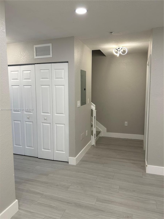 hallway with light wood-style flooring, electric panel, visible vents, and baseboards