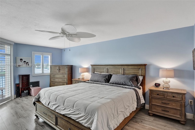 bedroom featuring baseboards, light wood-style flooring, a textured ceiling, and a ceiling fan