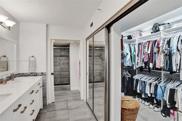 full bathroom featuring a walk in closet, visible vents, a sink, a textured ceiling, and double vanity