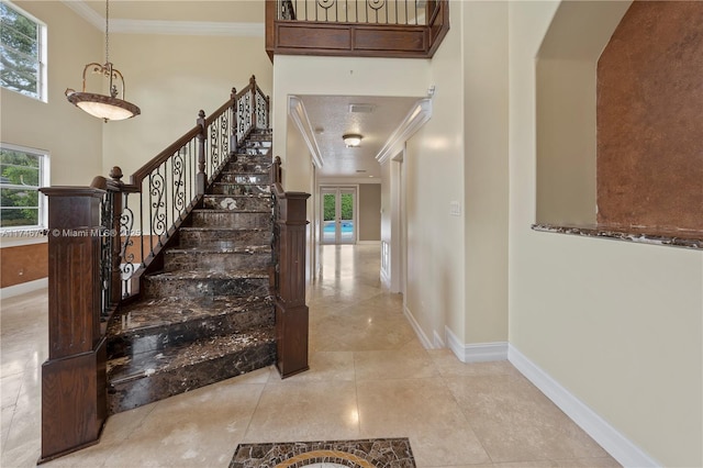 stairway with baseboards, a high ceiling, ornamental molding, and a wealth of natural light