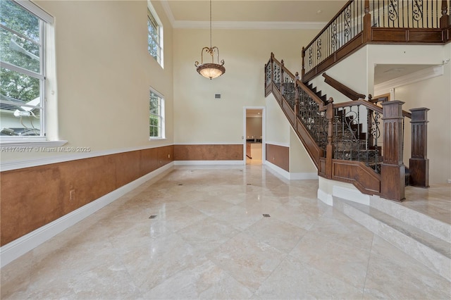 foyer entrance featuring stairway, a high ceiling, ornamental molding, and wainscoting