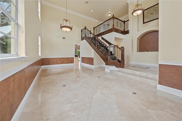 foyer featuring a wainscoted wall, ornamental molding, stairs, and a towering ceiling