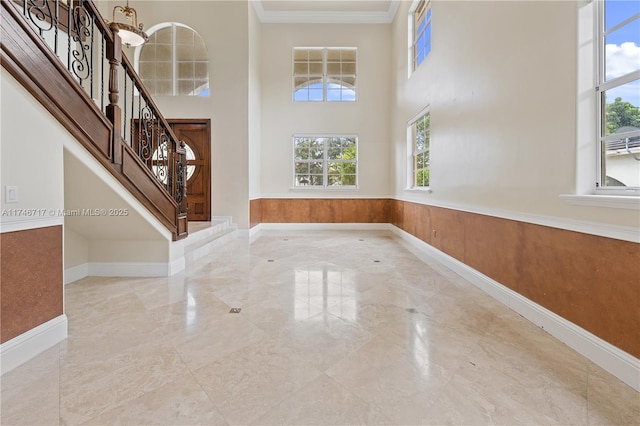 entryway featuring marble finish floor, a wainscoted wall, stairway, a high ceiling, and ornamental molding