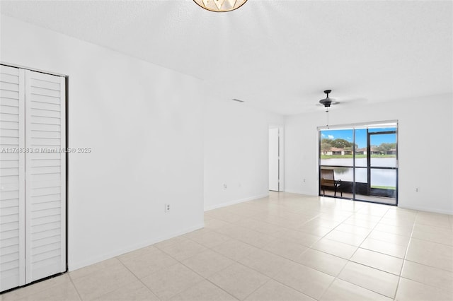 empty room with ceiling fan, light tile patterned floors, a textured ceiling, and baseboards