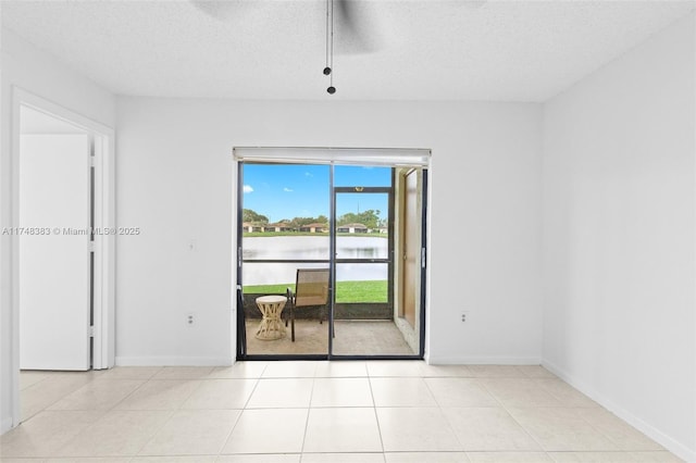 empty room with a water view, a textured ceiling, baseboards, and light tile patterned floors