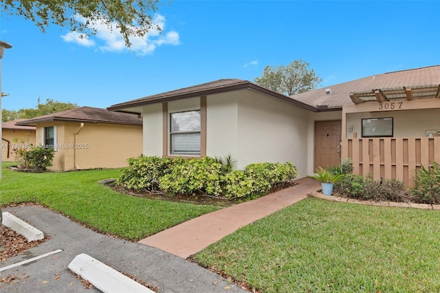 view of front of home featuring fence, a front lawn, and stucco siding