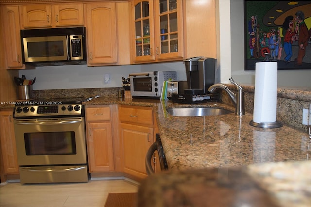 kitchen featuring a toaster, stainless steel appliances, glass insert cabinets, a sink, and dark stone counters