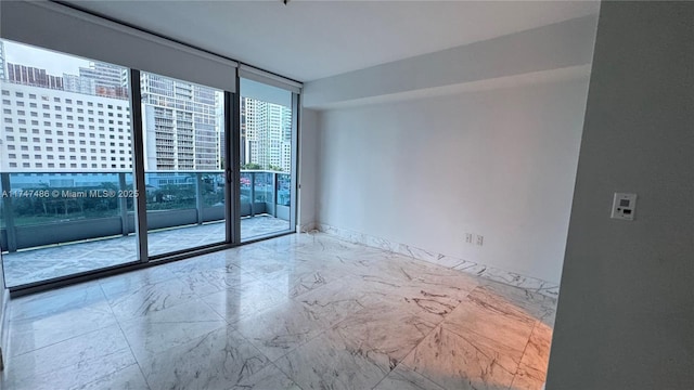 empty room featuring a wall of windows, marble finish floor, a city view, and baseboards