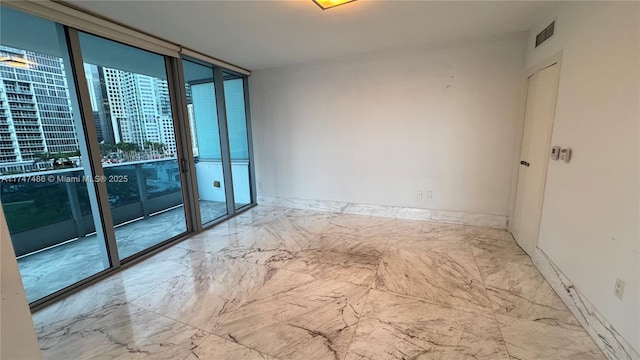 spare room featuring baseboards, marble finish floor, visible vents, and floor to ceiling windows