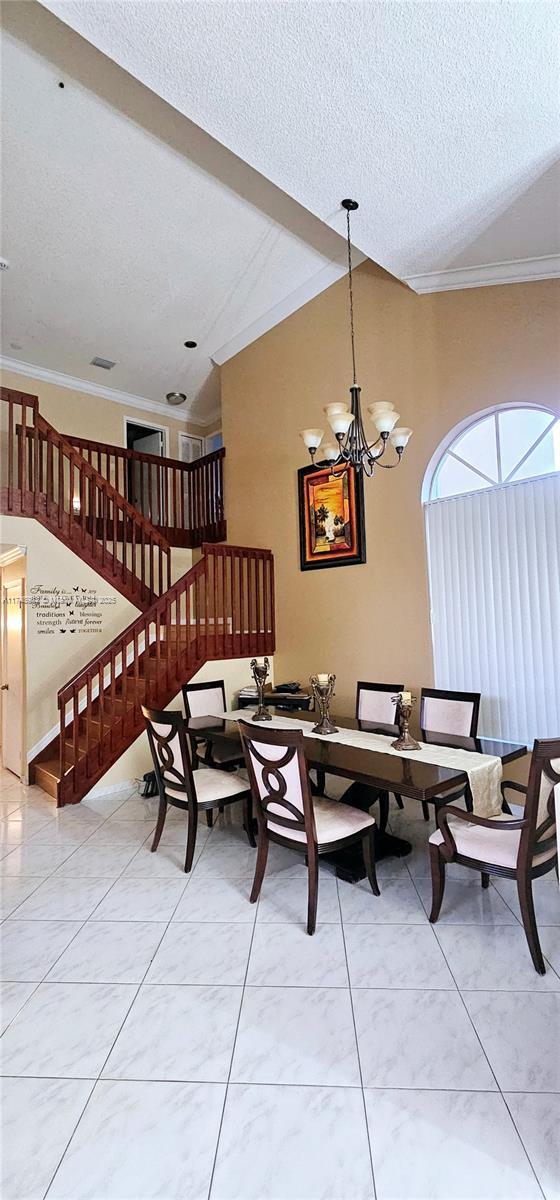 dining room featuring a textured ceiling, ornamental molding, stairway, and a notable chandelier