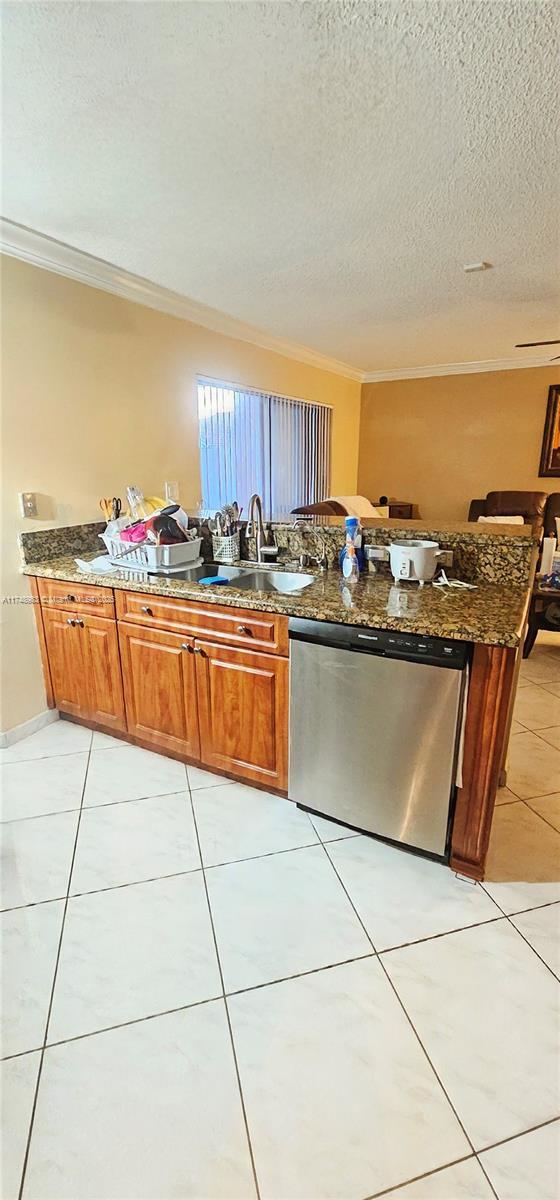 kitchen with dishwasher, brown cabinetry, and dark stone countertops