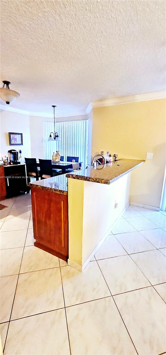 kitchen featuring dark countertops, light tile patterned floors, ornamental molding, and pendant lighting