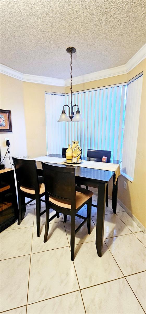 dining area with baseboards, ornamental molding, tile patterned floors, a textured ceiling, and a notable chandelier