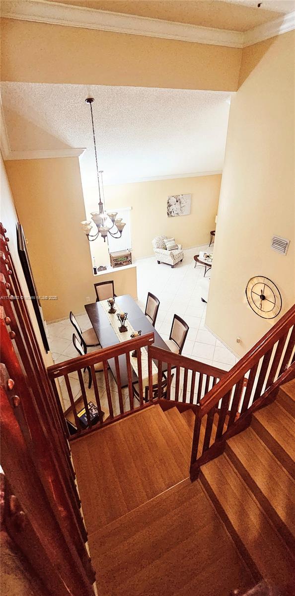 stairs featuring ornamental molding, a chandelier, a textured ceiling, and wood finished floors