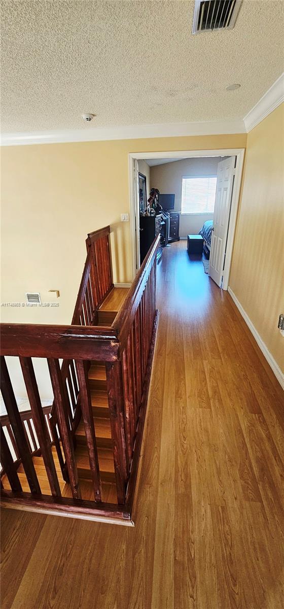 18860 NW 12th St, Pembroke Pines, FL 33029 - hallway featuring wood finished floors, a textured ceiling, an upstairs landing, ornamental molding, and baseboards