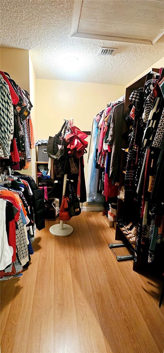 walk in closet featuring visible vents, wood finished floors, and attic access