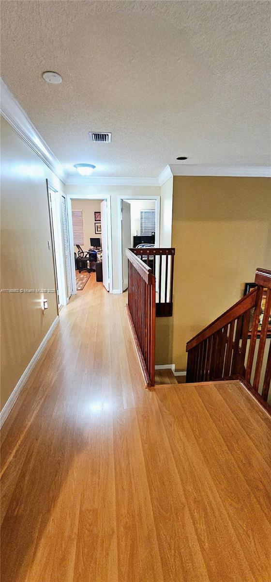 corridor featuring a textured ceiling, wood finished floors, an upstairs landing, and crown molding