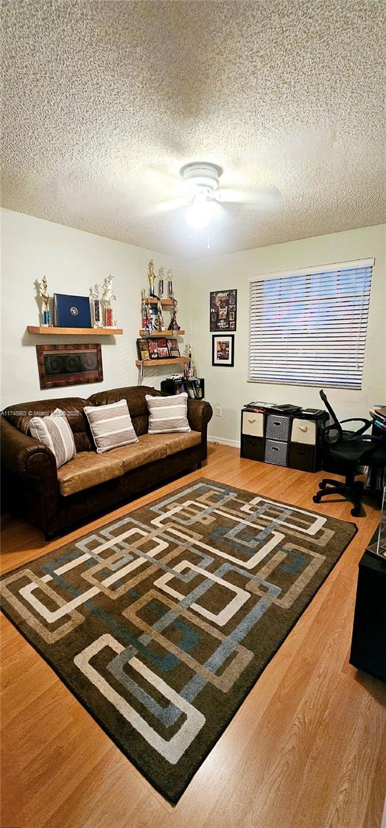 living room with ceiling fan, a textured ceiling, and wood finished floors