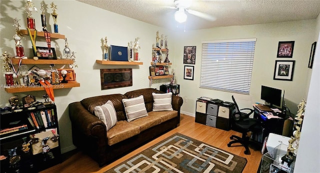 office area featuring a textured ceiling, a fireplace, wood finished floors, a ceiling fan, and baseboards