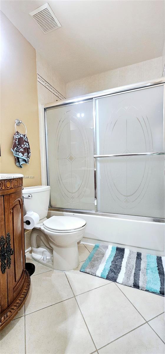 bathroom featuring toilet, tile patterned flooring, visible vents, and combined bath / shower with glass door