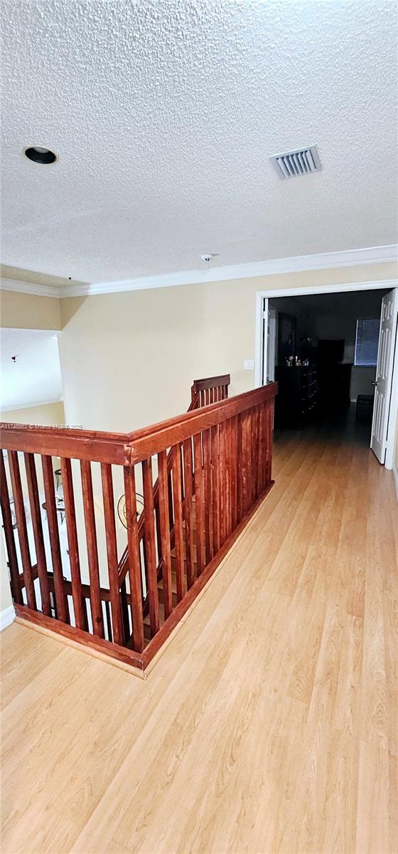 corridor featuring light wood finished floors, visible vents, and ornamental molding