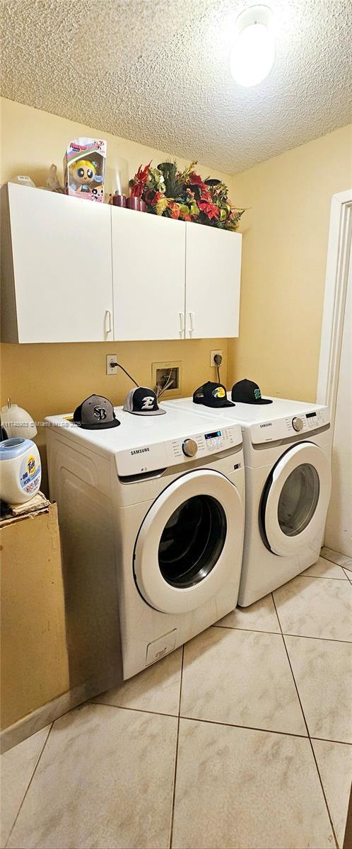 laundry area with cabinet space, washer and clothes dryer, a textured ceiling, and light tile patterned flooring