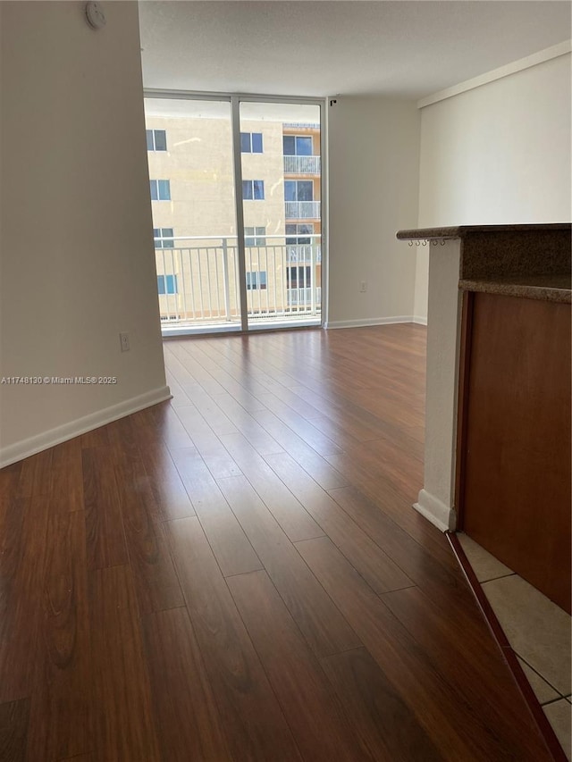 unfurnished living room featuring a wall of windows, baseboards, and wood finished floors