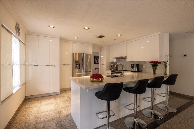 kitchen with modern cabinets, a peninsula, stainless steel fridge with ice dispenser, and a sink