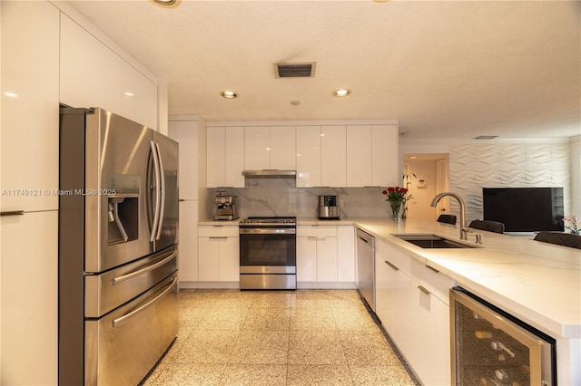 kitchen featuring a peninsula, a sink, wine cooler, appliances with stainless steel finishes, and modern cabinets