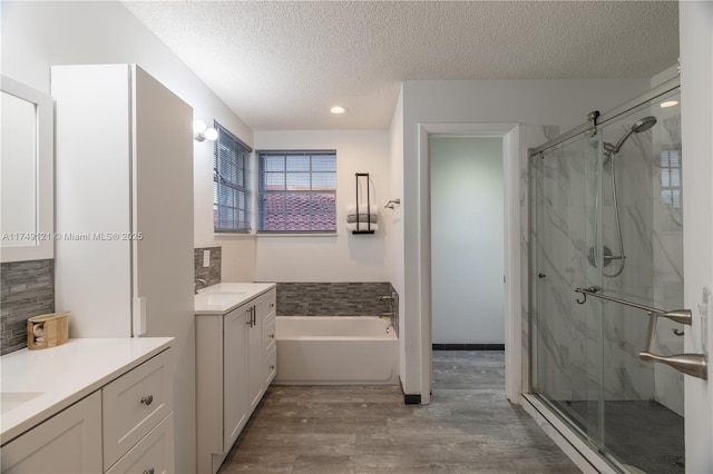 full bath with a stall shower, wood finished floors, a textured ceiling, and two vanities